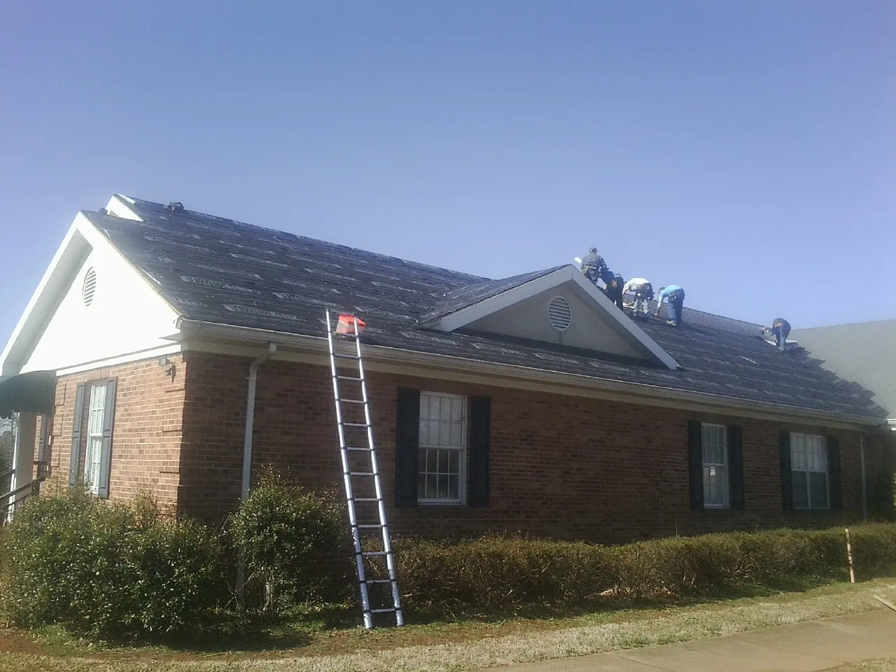 Crew tearing shingles off a brick ranch roof with a ladder set — Emergency Roof Repair work by our crew in Crestline