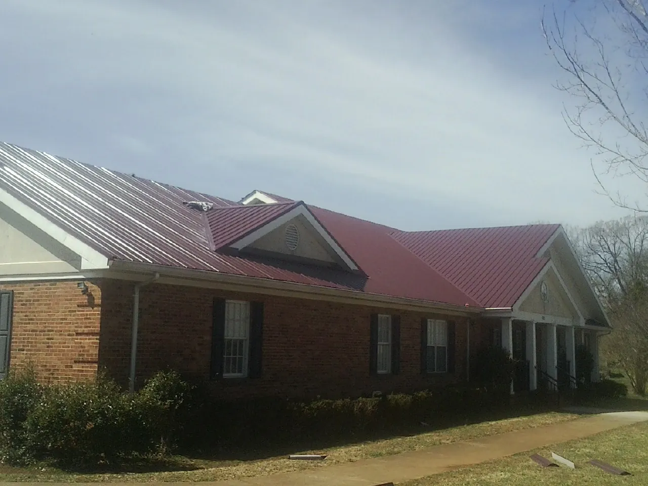 Red metal roof with gabled entries on a long brick building, from a Hail Damage Roof Repair job in Crestline