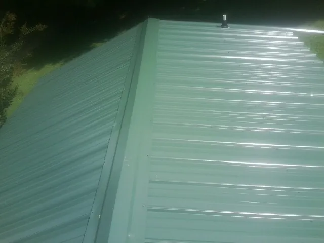 New green metal panels meeting at the ridge of a roof — Flat Roof Repair work by our crew in Crestline