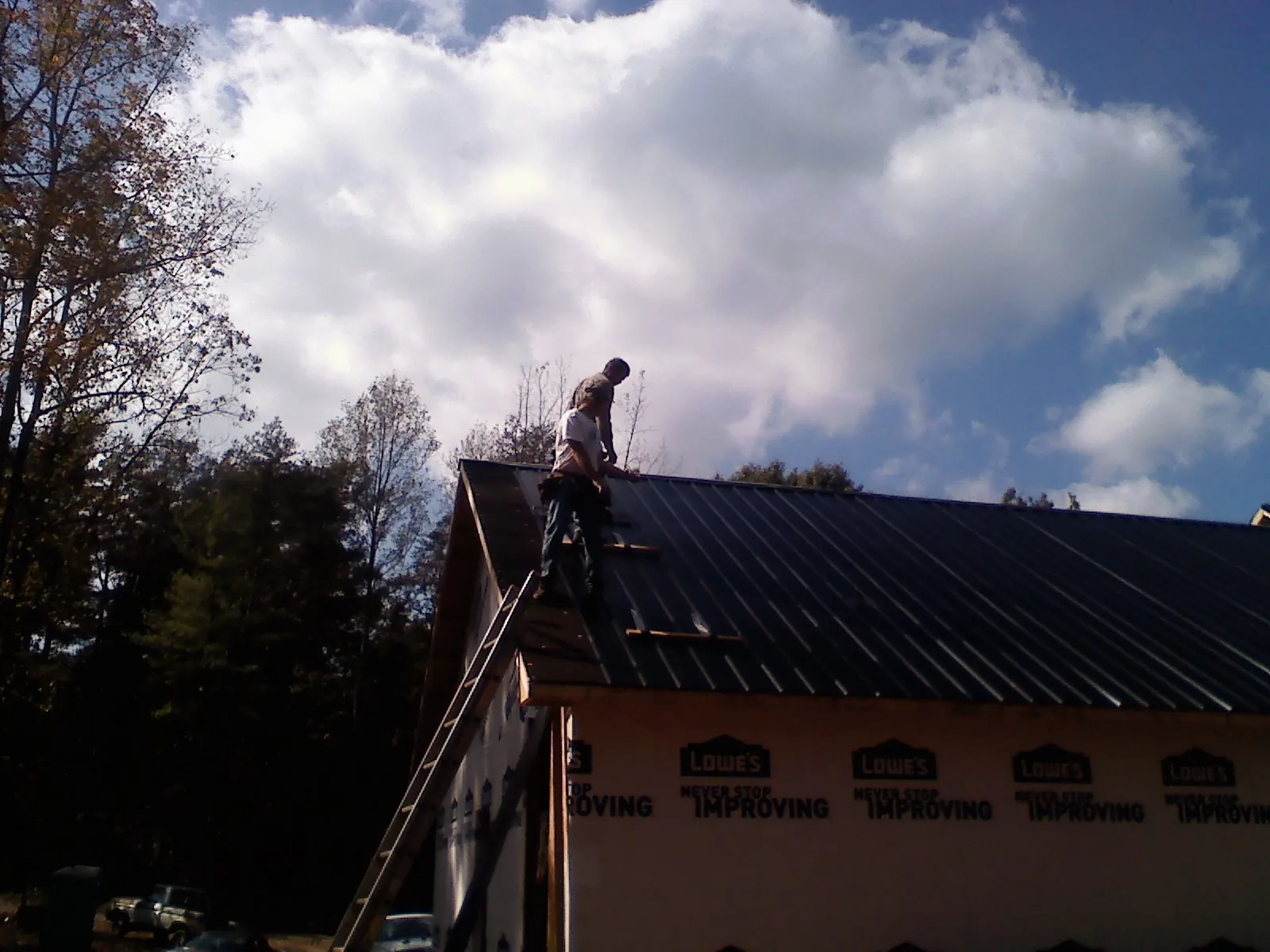 Roofer fastening dark metal panels high against a cloudy sky, from a Roof Inspection job in Crestline