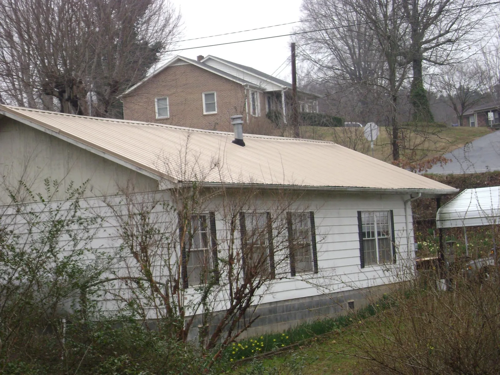 Tan metal roof on a white sided house set into a hillside — Commercial Roofing by Roofing Brothers in Crestline